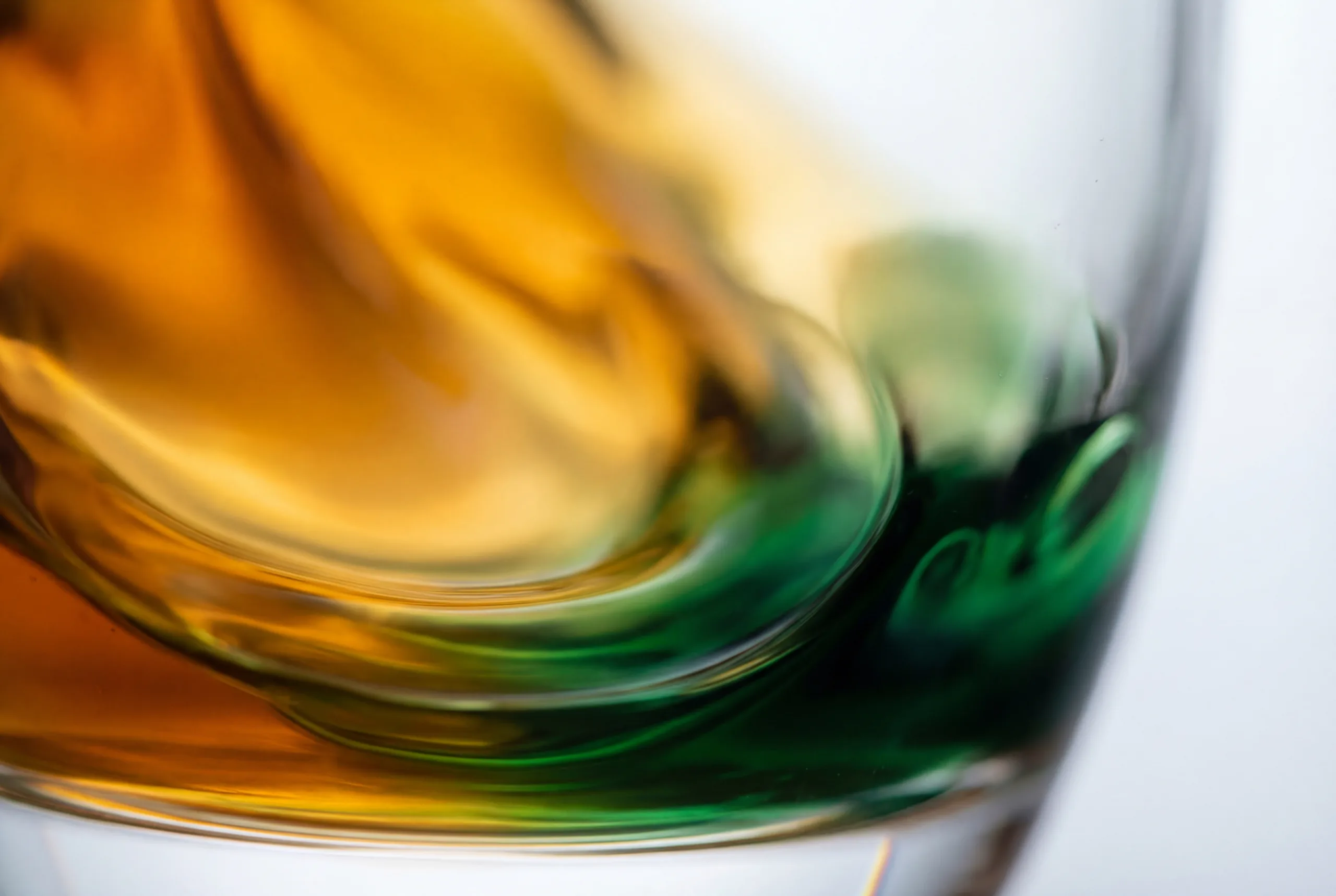 Close-up macro of amber and green fuel additive liquid swirling in a glass vessel