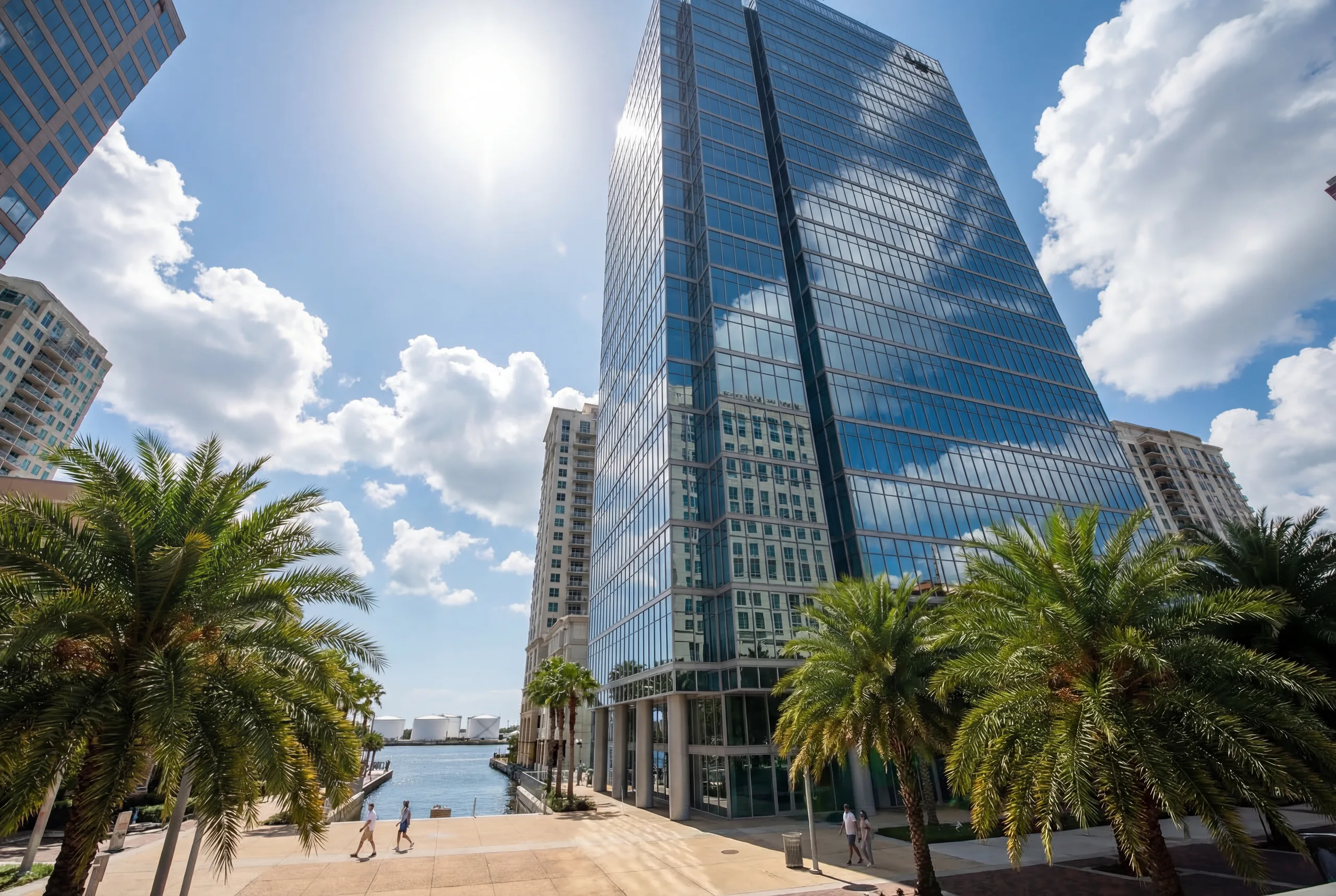 Modern glass office tower with palm trees along a waterfront promenade in downtown Tampa